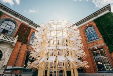 a pavilion in the courtyard of a museum made from dozens of white and timber folding deck chairs in a tall cylinder form