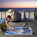 artist Ellie Hannon working on a painting on the aft deck of a research vessel at sunset