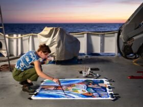 artist Ellie Hannon working on a painting on the aft deck of a research vessel at sunset