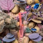 a detail of a large cardboard sculpture of a coral reef, focusing on a sea turtle and numerous small fish