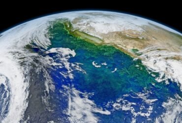 Satellite composite image of the California coast and Pacific Ocean with varying colors of blues and greens where there are phytoplankton blooms. The curve of the Earth can be seen at the top of the image