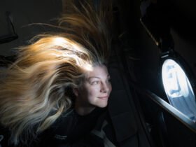 a woman with blonde hair that floats near a window overlooking earth from above