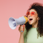 Woman against a pink background holding a megaphone