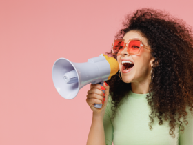 Woman against a pink background holding a megaphone