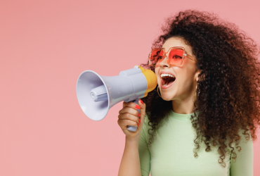 Woman against a pink background holding a megaphone