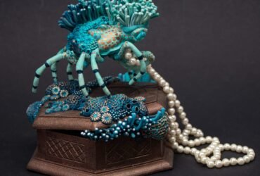 a sculpture made from a vintage box with a decorator crab on top, collecting a string of pearls and surrounded by blue coral