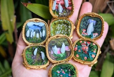 an outstretched palm holds gold open compacts with tiny garden scenes and ghosts inside