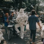 a photograph of a person standing next to a motorbike, wearing a handmade costume made from white plastic yarn, with woven arms and legs and a torso-head design that resembles coral textures