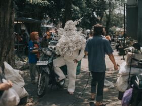 a photograph of a person standing next to a motorbike, wearing a handmade costume made from white plastic yarn, with woven arms and legs and a torso-head design that resembles coral textures