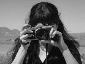 a black-and-white portrait of an anonymous woman taking a photo with an SLR camera with the desert in the background