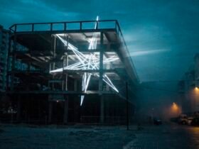 a monumental public art installation of a star shape made from LED strips inside of a concrete and steel building at night