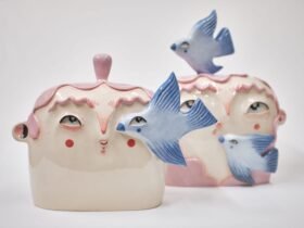 two ceramic sculptures of cute heads and faces with pink hair, with bluebirds flying around them