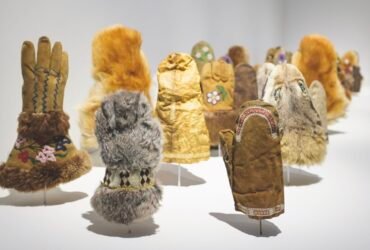 a detail of an installation of various handmade fur and seal skin mittens illuminated in a gallery