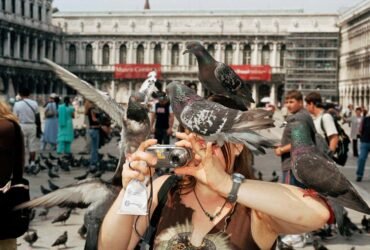 ITALY. Venice. A tourist takes a picture while pigeons surround her. 2005.