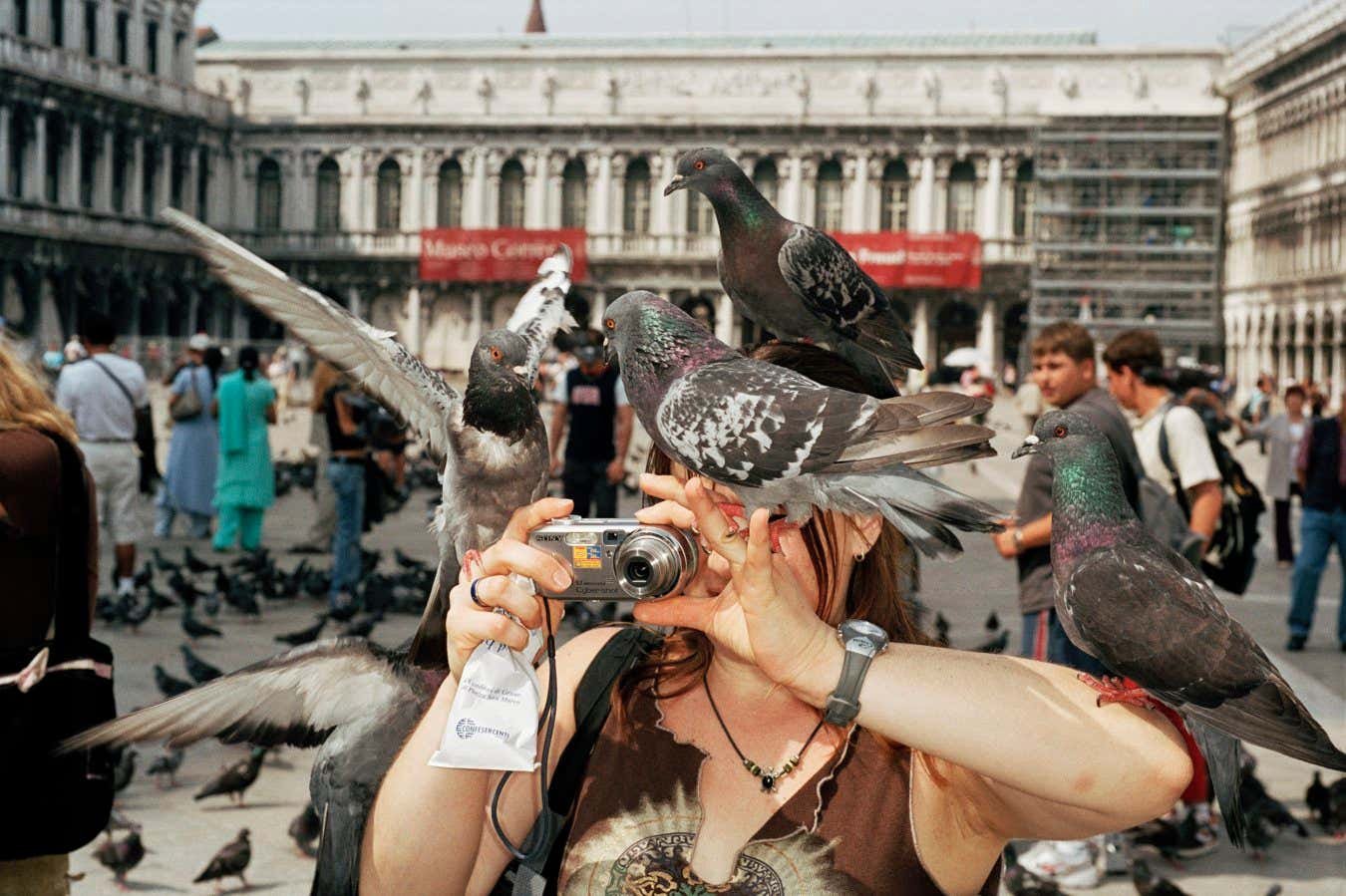 ITALY. Venice. A tourist takes a picture while pigeons surround her. 2005.