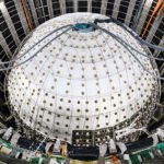 A sphere inside a large pit is covered in white sheeting with tubes entering a hole in the top.