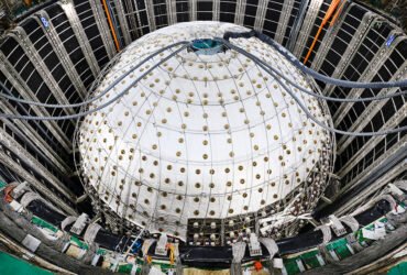 A sphere inside a large pit is covered in white sheeting with tubes entering a hole in the top.