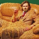 a portrait of a man in a brown suit, sitting on a brown leather couch, covered in spaghetti