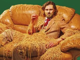 a portrait of a man in a brown suit, sitting on a brown leather couch, covered in spaghetti