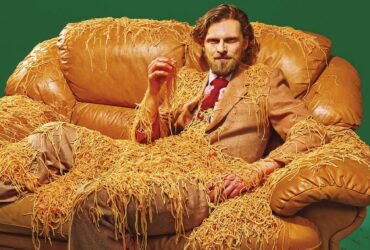 a portrait of a man in a brown suit, sitting on a brown leather couch, covered in spaghetti