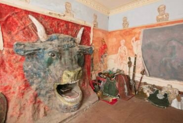 the interior of Ron Gittins' apartment in Birkenhead, England, featuring a very ornate, hand-sculpted fireplace of a bull's head with murals all around on the walls