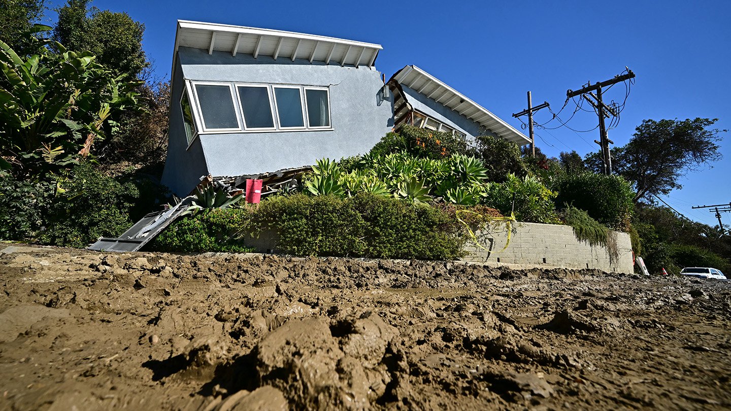 A wrecked house is in the background, while mud fills the foreground