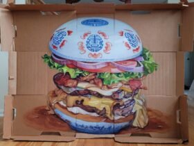 a painting of a juicy drippy burger with a blue and white porcelain style motif on the bun all on a cardboard box