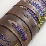 a detail of a long, rusted, pipe-like sculpture with cross-stitched flowers along the surface