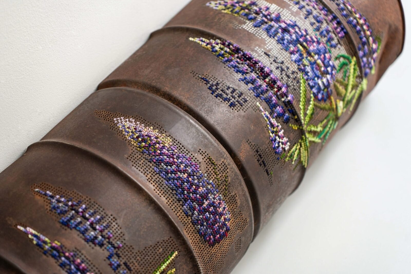 a detail of a long, rusted, pipe-like sculpture with cross-stitched flowers along the surface