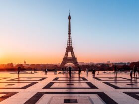 An orange sun reflects light on the smooth plaza in front of the Eiffel Tower in Paris.