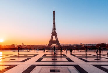 An orange sun reflects light on the smooth plaza in front of the Eiffel Tower in Paris.