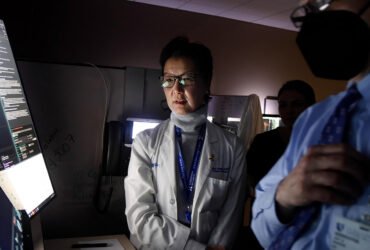 Shelley Hwang wears a lab coat. Her face is illuminated by light from a computer screen where she reviews results from breast cancer testing.