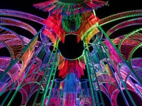a detail of a vibrantly colored architectural pavilion made of metal poles and rope at night