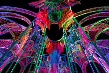 a detail of a vibrantly colored architectural pavilion made of metal poles and rope at night