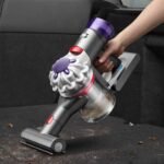 Handheld vacuum being used to clean up leaves in the back of a car