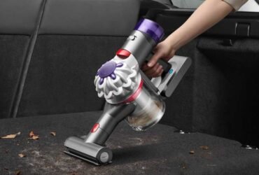 Handheld vacuum being used to clean up leaves in the back of a car