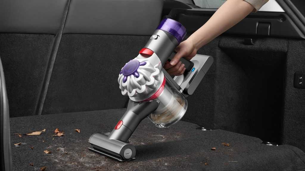 Handheld vacuum being used to clean up leaves in the back of a car