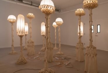 a group of sculptural white lamps made from pieces of fabric coated in bio resin and knotted, illuminated and displayed in a white gallery space