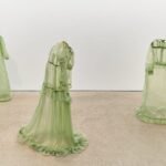 a collection of stiff green fiberglass victorian style dresses standing without wearers in the middle of a gallery