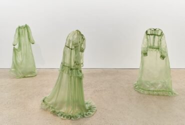 a collection of stiff green fiberglass victorian style dresses standing without wearers in the middle of a gallery