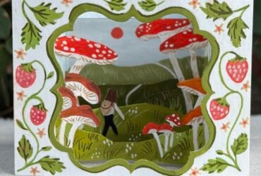 a small paper tunnel book depicting large mushrooms and a figure hiking through a landscape