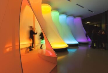 a large-scale fabric installation in a museum with different segments illuminated in the colors of a prism