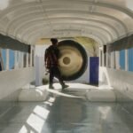 the artist standing next to a large gong in the cab of an empty bus