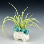 a porcelain sculpture that resembles a bundle of textile with frills, with bright green grass-like spikes or fronds emerging from it