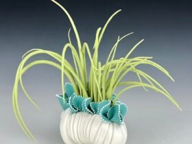 a porcelain sculpture that resembles a bundle of textile with frills, with bright green grass-like spikes or fronds emerging from it