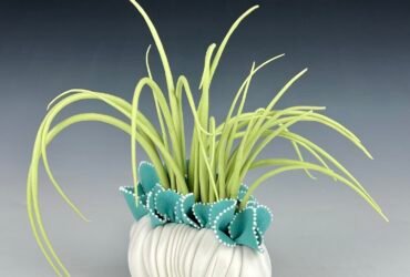 a porcelain sculpture that resembles a bundle of textile with frills, with bright green grass-like spikes or fronds emerging from it