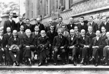 A black and white photo of nearly 30 physicists, most seated, some standing, posing for the camera.