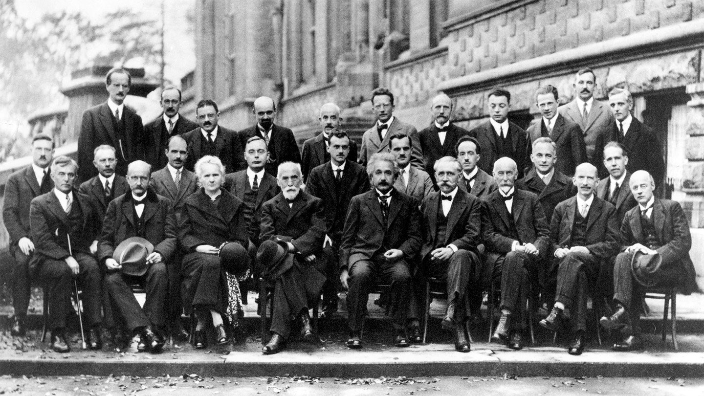 A black and white photo of nearly 30 physicists, most seated, some standing, posing for the camera.