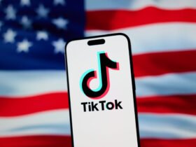 The TikTok app and logo are seen on a mobile device in front of a US flag