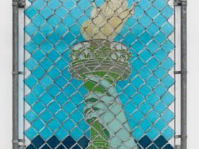 a wall sculpture of stained glass depicting the arm of the Statue of Liberty, installed behind a chainlink gate